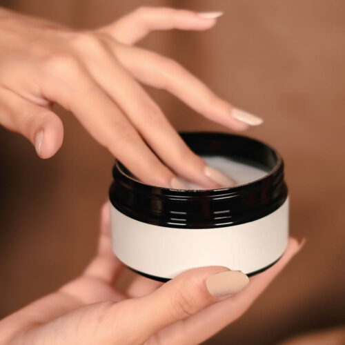Hands holding an open jar of cleansing balm