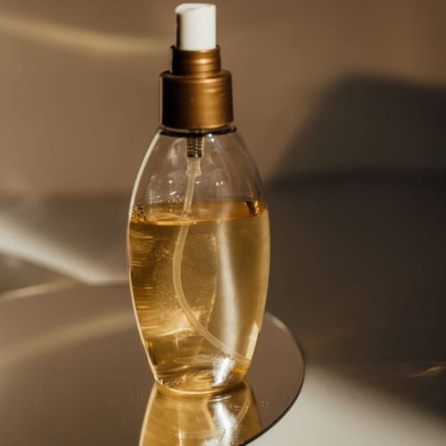 Glass bottle of golden face oil on a mirrored dish