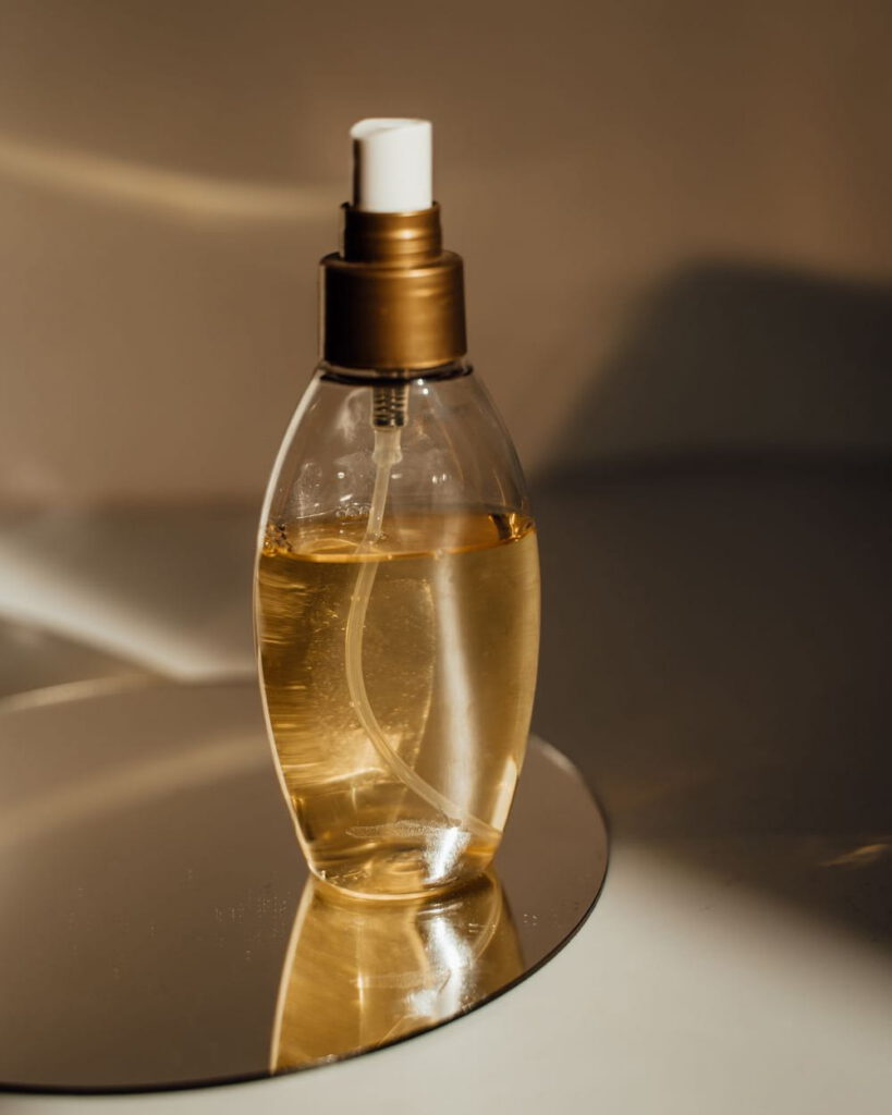 Glass bottle of golden face oil on a mirrored dish